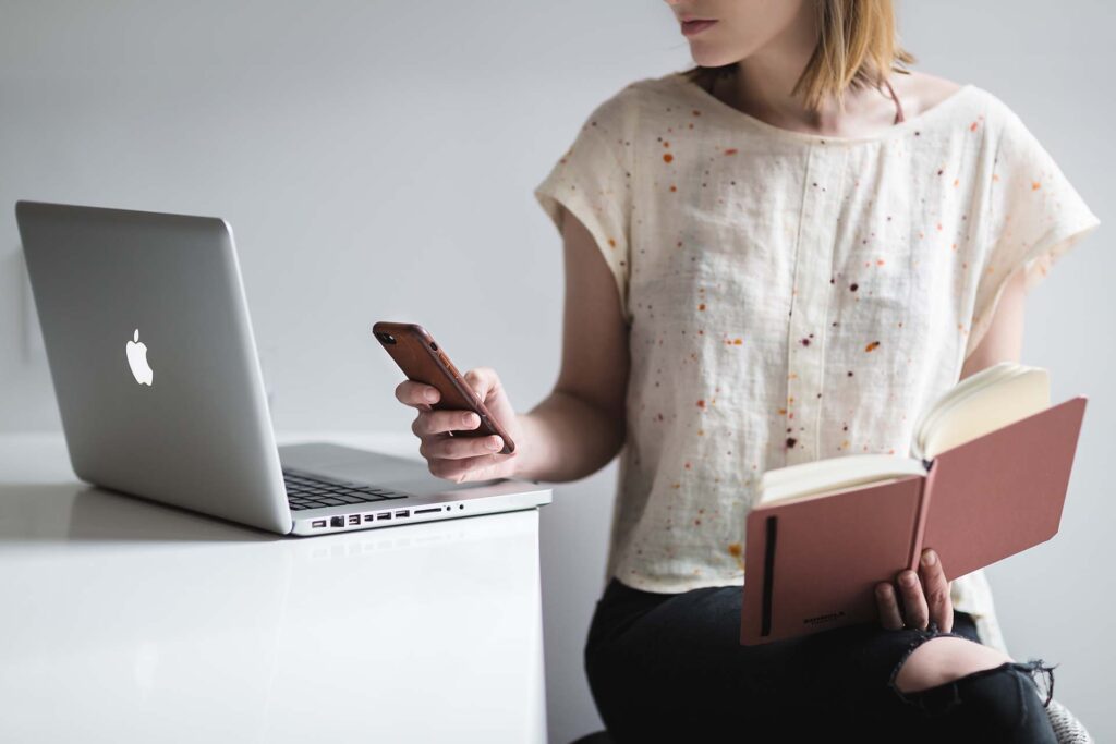 A woman sitting with a laptop, book, and phone in hand