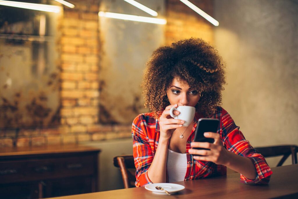 Young woman looking at her phone and drinking coffee