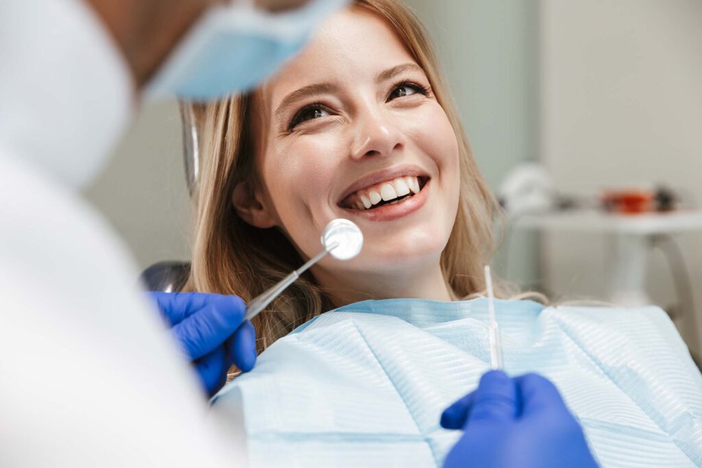 Image of pretty young woman sitting in dental chair at medical center while professional doctor fixing her teeth