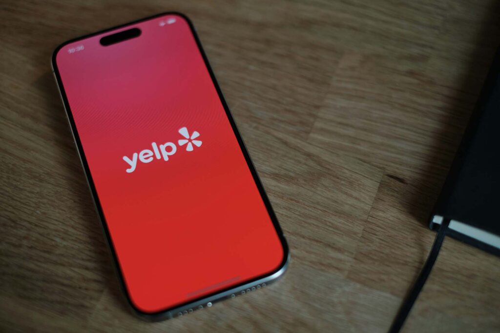 A phone on a wooden table with a Yelp logo on the screen 